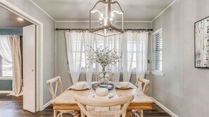 Un coin repas comprenant une table en bois, six chaises, un lustre et un vase avec des fleurs.