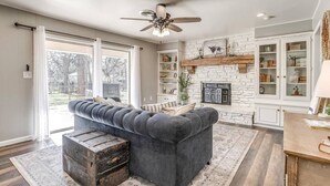 Un salon avec un canapé gris foncé, une commode en bois, une cheminée et un ventilateur de plafond.