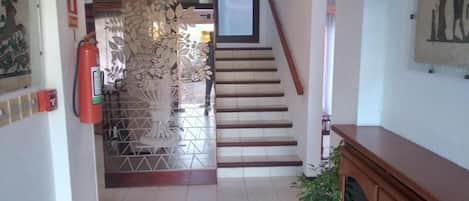 A hallway with a staircase, a fire extinguisher, and a potted plant.