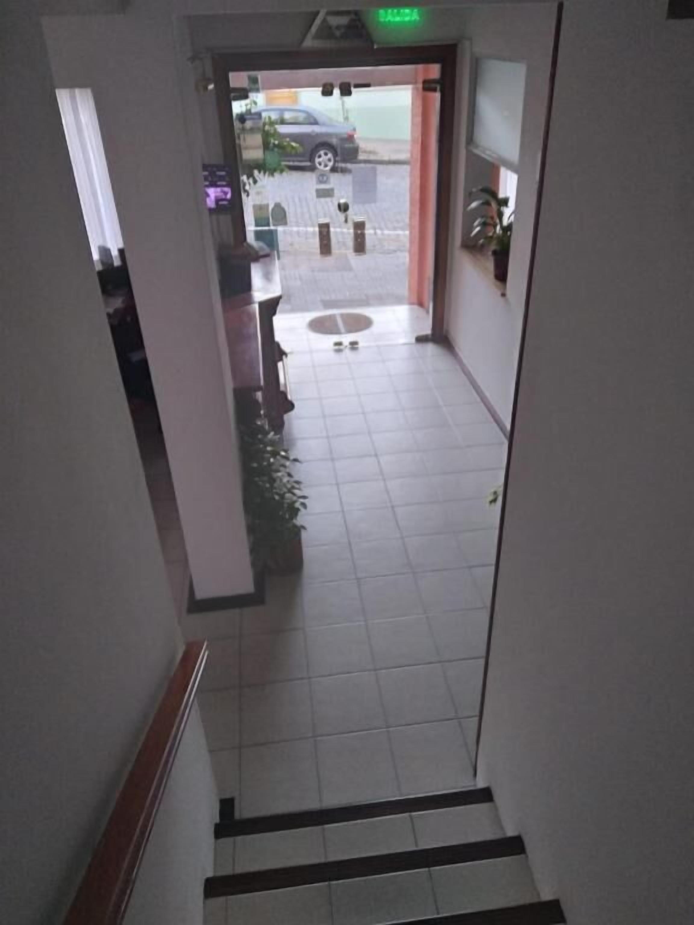 Entrada de hotel con suelo de baldosas, un mostrador de recepción y un estacionamiento visible a través de las puertas de vidrio.