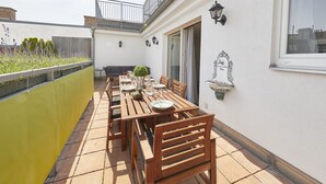 A patio with a wooden table and chairs, a yellow fence, and a white wall with a window and wall-mounted lights. - Your rooftop penthouse in Vienna 2 (Wien)