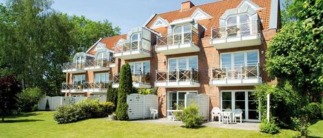 A multi-story residential building with balconies, a well-maintained lawn, and a brick facade.