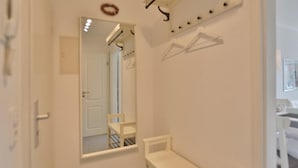 Une salle de bain avec un miroir, un banc blanc, un porte-serviettes et une porte.