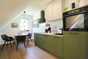 A modern kitchen with green cabinets, a black oven, and a dining area with two chairs and a table. - Am Rosenhain 23 Appartement 5 (Timmendorfer Strand)