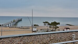 Une plage avec une jetée qui s’avance dans l’eau, une petite construction près de la plage et un arbre au premier plan.