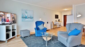 Un salon moderne avec un téléviseur, deux fauteuils, une table basse et un tableau accroché au mur.
