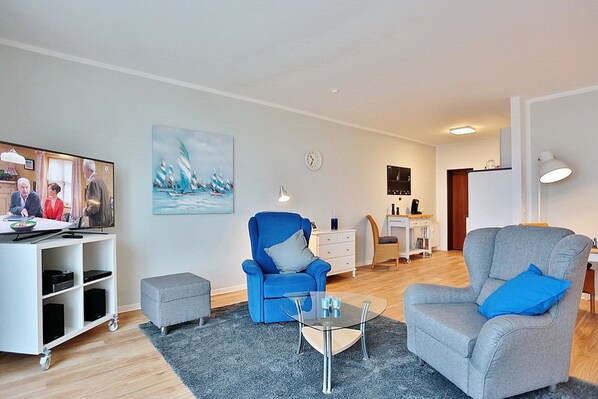 Ein modernes Wohnzimmer mit Fernseher, zwei Sesseln, einem Couchtisch und einem Gemälde an der Wand.