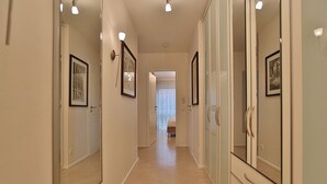 A hallway with a bed at the end, framed pictures on the walls, and a wardrobe with a mirror. - Wohldkamp 4 Appartement 4 (Timmendorfer Strand)