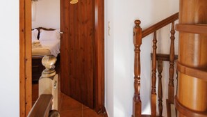 Una escalera de madera con barandilla que conduce a un dormitorio con cama y mesita de noche.