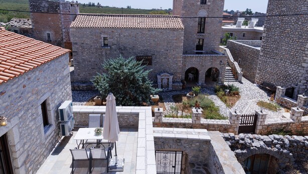 Un patio con edificios de piedra, una torre, y una mesa con sillas y una sombrilla.