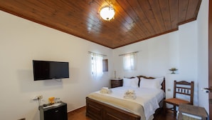 Un dormitorio con techo de madera, televisor de pantalla plana, cama con ropa blanca, mesita de noche y una silla.