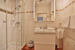 Uma casa de banho moderna com chuveiro em cabine de vidro, lavatório com espelho em cima e porta-toalhas.