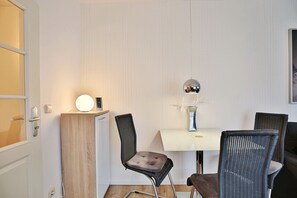 Quarto compacto com mesa de jantar, duas cadeiras, um armário pequeno e uma luminária fixada na parede.