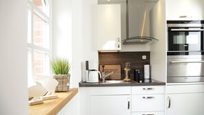A modern kitchen with white cabinetry, a built-in oven, and a coffee maker. - Am Rosenhain Appartement 3 Hygge (Timmendorfer Strand)