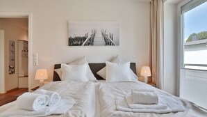 Habitación de hotel con dos camas, ropa de cama blanca, un cuadro de un puente y una ventana con cortinas.