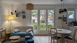 A modern living room with a sofa, coffee table, and dining table. There is a large window with a view of trees and buildings. - Spacious quiet nest with garden near the sea (La Tranche-sur-Mer)