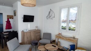 A compact living space with a TV, a wooden cabinet, a sofa, a dining table, and a window with a view. - Spacious quiet nest with garden near the sea (La Tranche-sur-Mer)