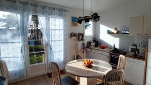A kitchen with a dining table, chairs, a refrigerator, and a window with curtains. - Spacious quiet nest with garden near the sea (La Tranche-sur-Mer)