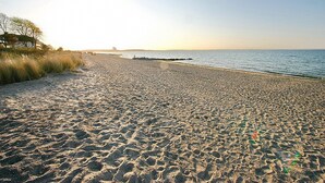 Une plage de sable fin, un ciel dégagé, une vue lointaine d’un bâtiment et une mer calme.