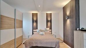 Une chambre moderne avec un grand lit, des murs recouverts de panneaux en bois et un éclairage encastré.