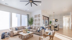 Ein geräumiges Wohnzimmer mit einer großen Couch, einem Couchtisch und Korbstühlen. Ein Essbereich mit Tisch und Stühlen lädt zum Verweilen ein, und ein großes Fenster sorgt für natürliches Licht.