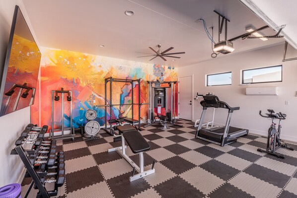 A gym with various exercise equipment, a checkered floor, and a colorful mural on the wall. - 6BR Sleeps 18 - Pool, Gym, Pizza Oven & Courts (St. George)