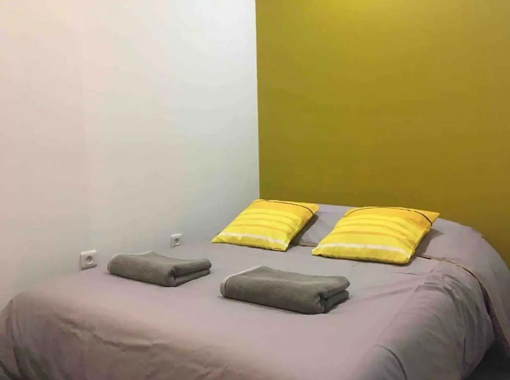 Un lit avec une couvre-lit grise et deux oreillers jaunes.