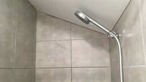 Douchegedeelte met een handdouche en betegelde wanden.