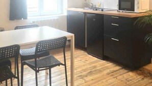 Een compacte keuken met donkere kastjes, een magnetron en een eethoek met een tafel en stoelen.