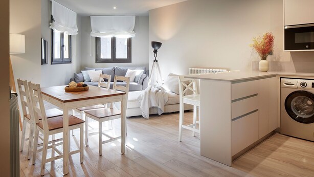 Un apartamento moderno con comedor, sala de estar con sofá y una mesa de centro, cocina con lavadora y un amplio ventanal con cortinas.