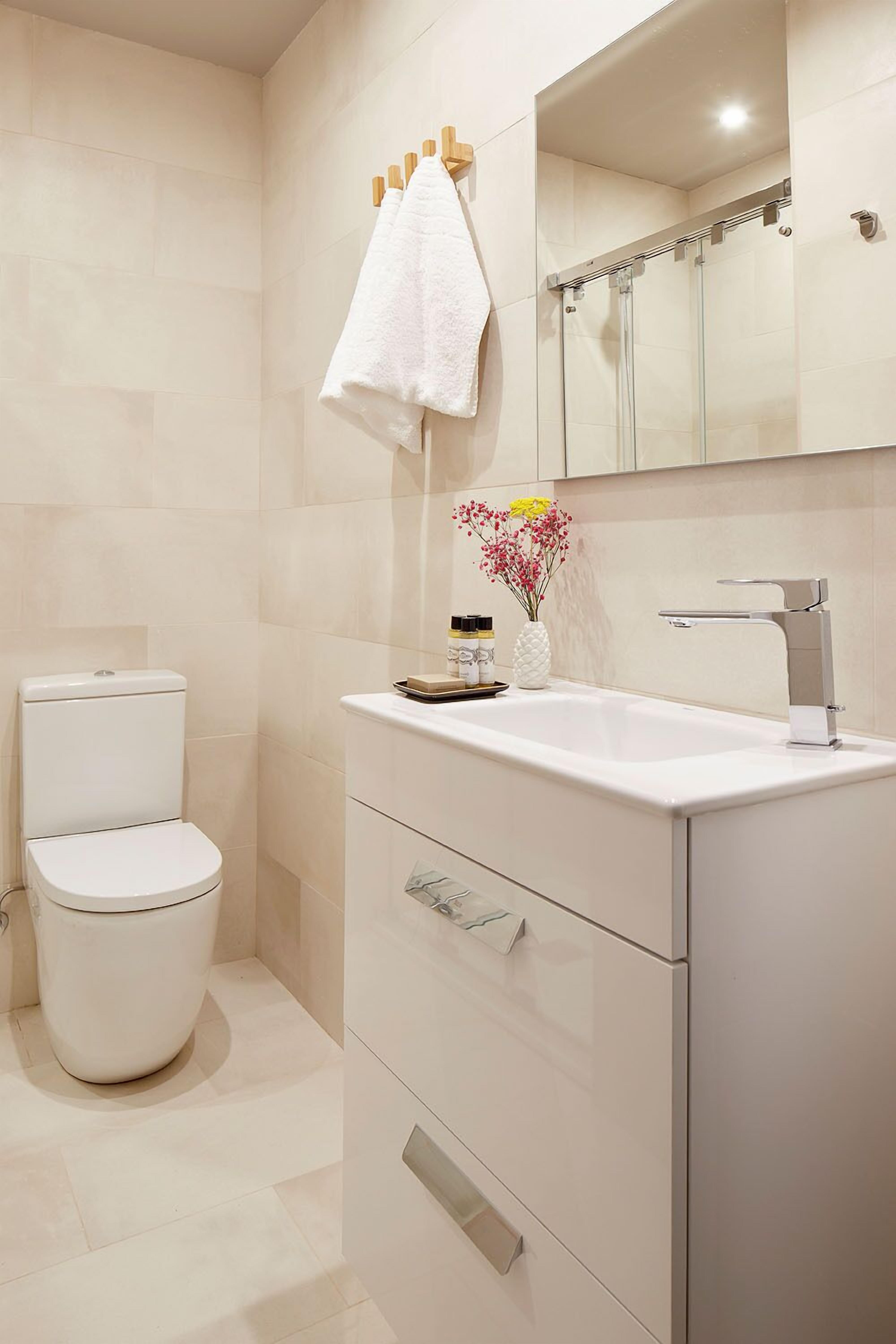 Une salle de bain moderne comprenant des toilettes, un lavabo avec un miroir au-dessus, et un espace douche.