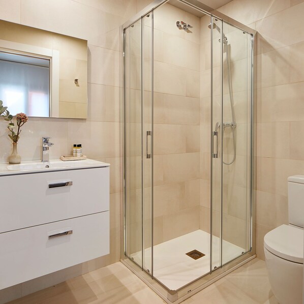 A modern bathroom with a glass-enclosed shower, a white sink with a mirror above, and a toilet.