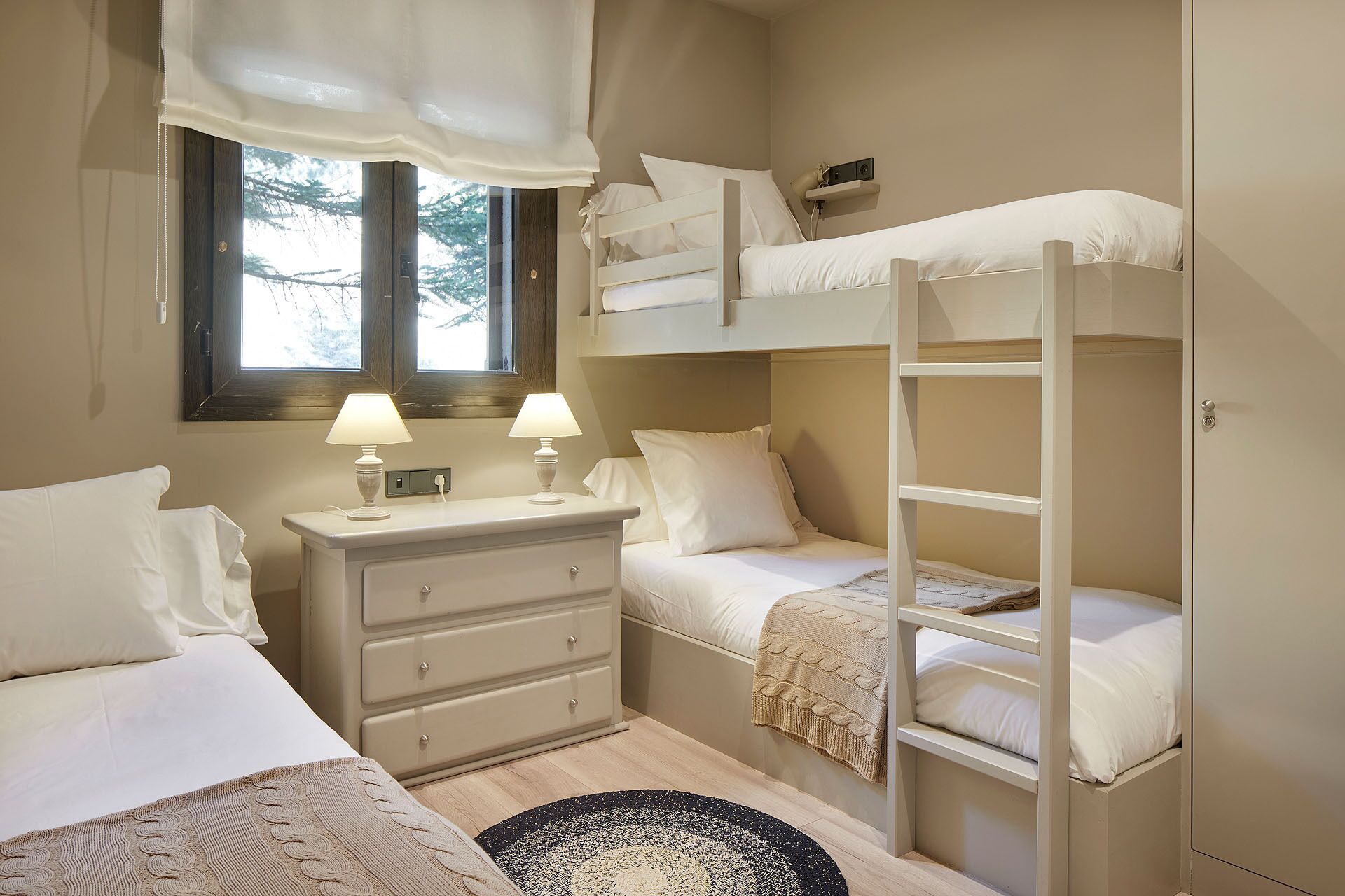 Une chambre avec des lits superposés, une table de chevet avec des lampes, une commode et une fenêtre avec des rideaux.