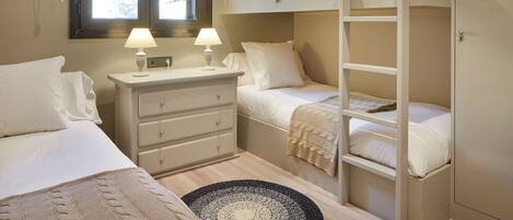 Une chambre avec des lits superposés, une table de chevet avec des lampes, une commode et une fenêtre avec des rideaux.