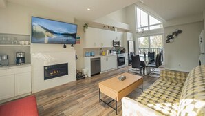 A modern kitchen with a fireplace, a dining area with a table and chairs, and a living room with a sofa.