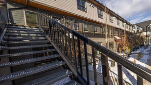 A staircase leading to a building with a metal railing, snow on the ground, and a clear sky.