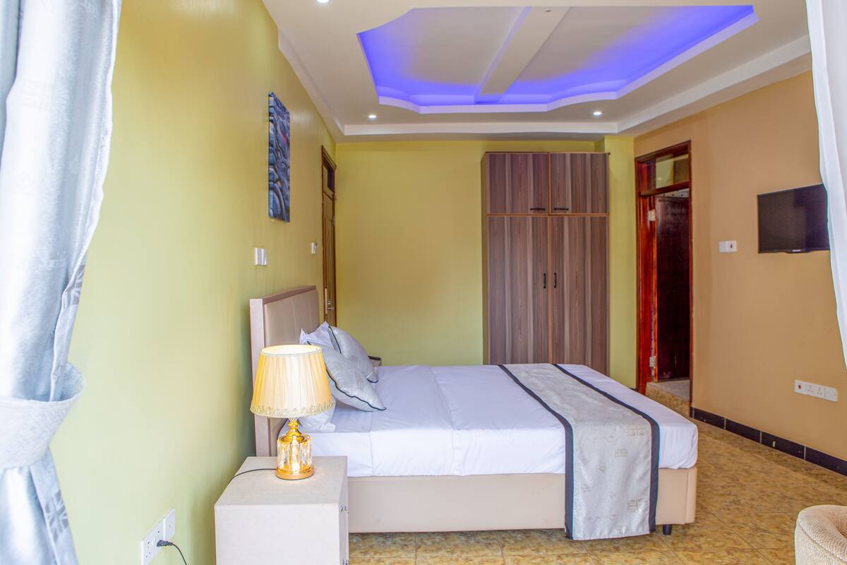 A bedroom with a bed, bedside lamp, wardrobe, and a television on the wall.