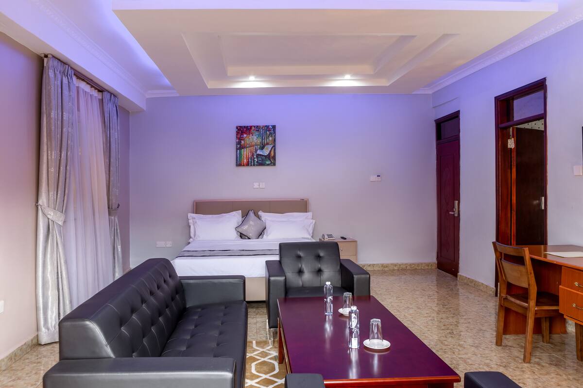 A hotel room with a bed, a sofa, a dining table, and a desk.