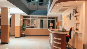 Una hall d'albergo con una reception, una scala e una pianta in vaso.