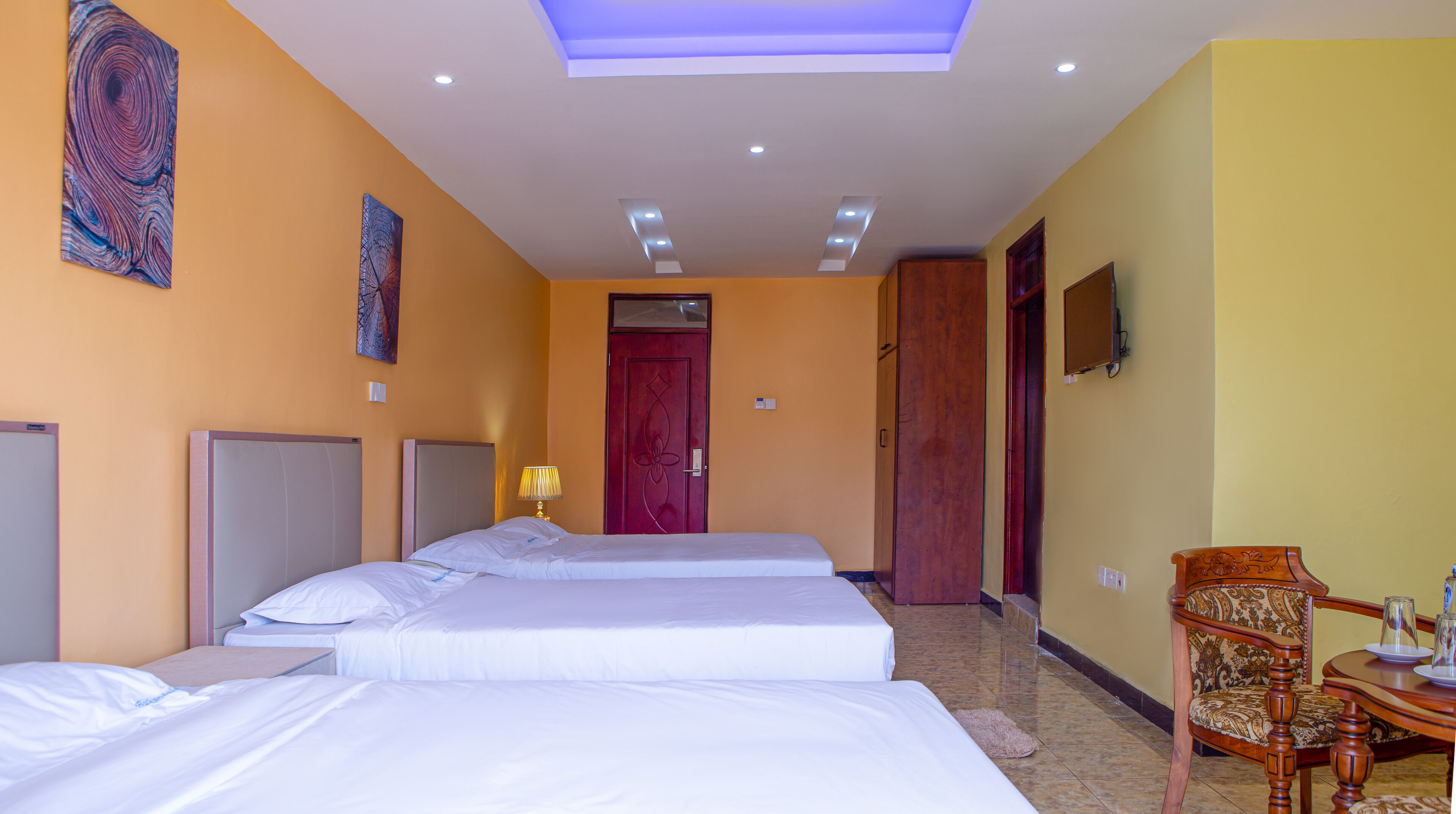 A hotel room with two beds, a wooden wardrobe, a desk, and a chair.