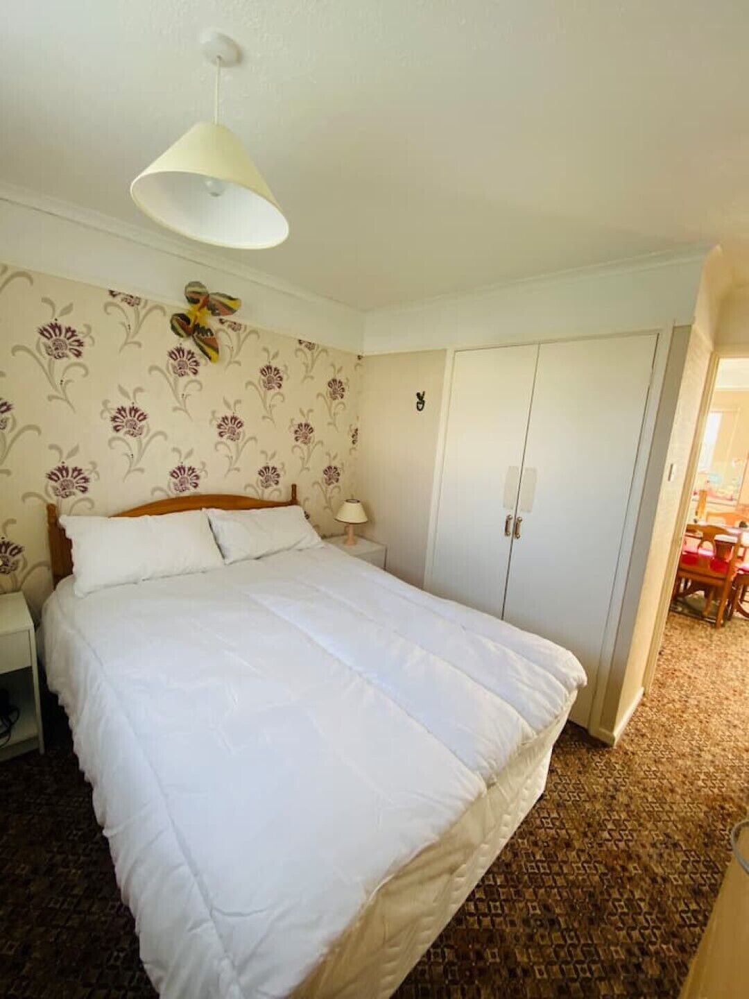 A bedroom with a large bed, a wardrobe, a nightstand, and a lamp.