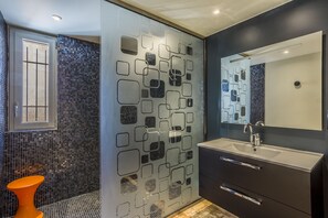 A modern bathroom with a large mirror, a sink, and a shower area with a unique geometric tile design.