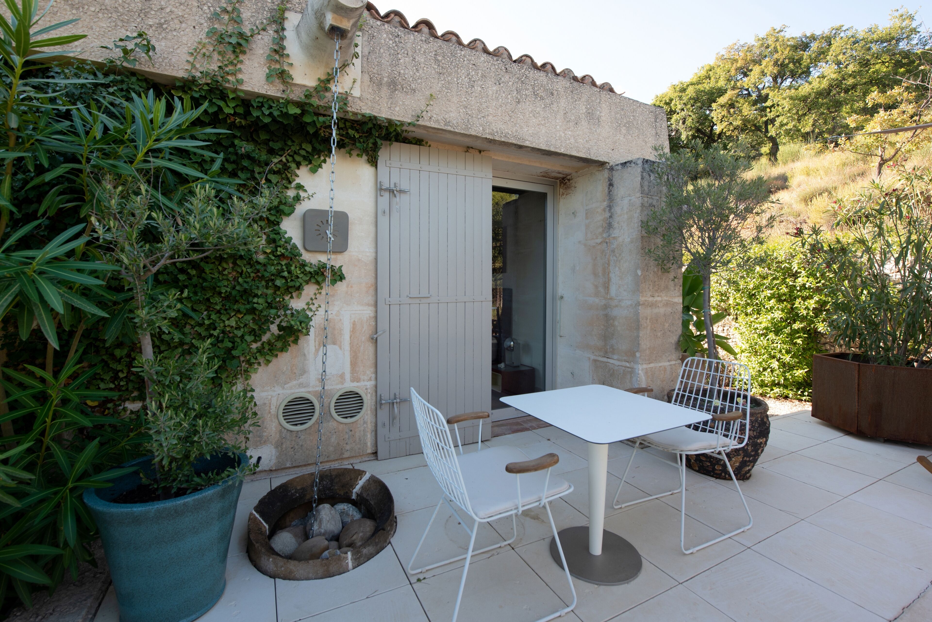 A patio with a white table and chairs, a potted plant, and a stone wall.