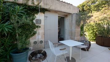 A patio with a white table and chairs, a potted plant, and a stone wall.