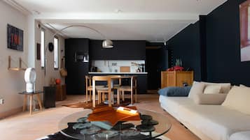 A modern living room with a glass coffee table, a sofa, and a dining area with chairs and a table.