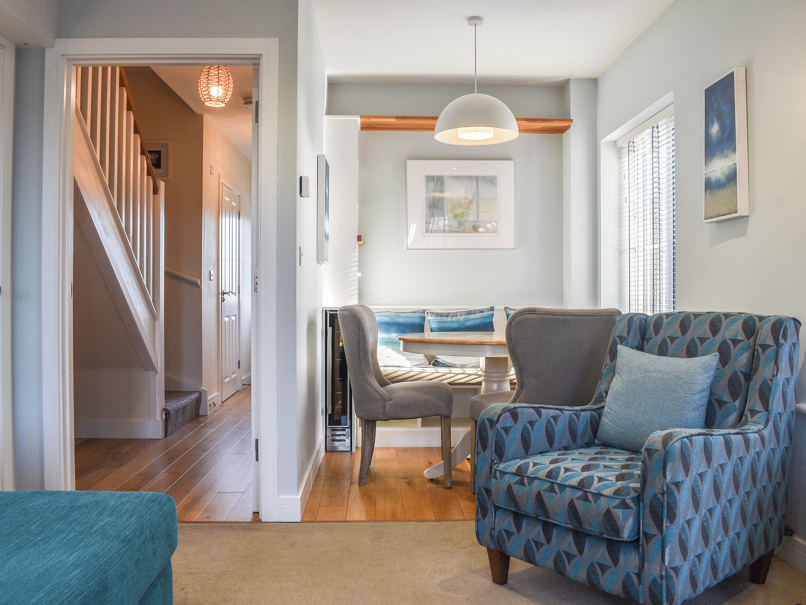 A modern living room with a patterned armchair, a dining table with chairs, and a staircase leading to another level.