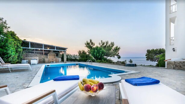 A poolside area with lounge chairs, a table with fruit, and a view of the sea. - A seafront villa with swimming pool (Achlia)