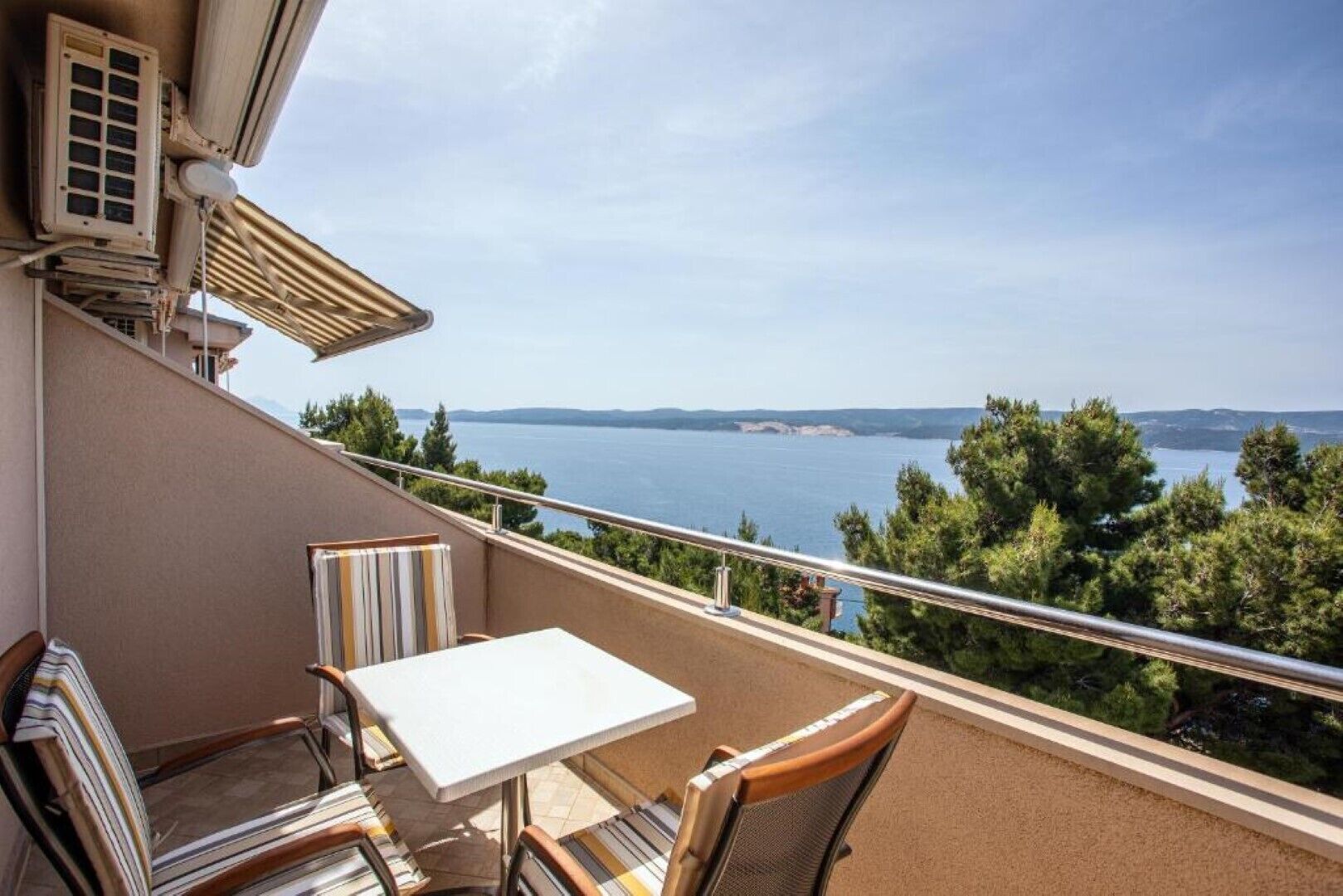 A balcony with a table and chairs, overlooking a body of water and distant land.