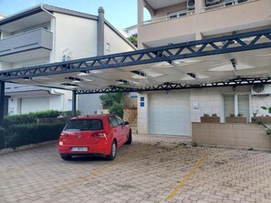 A red car parked under a covered parking area with a garage door and a stone wall with planters.