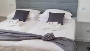 Un letto rifatto con lenzuola bianche e una testiera grigia, una foto incorniciata di una nave sulla parete e una coperta grigia sul letto.